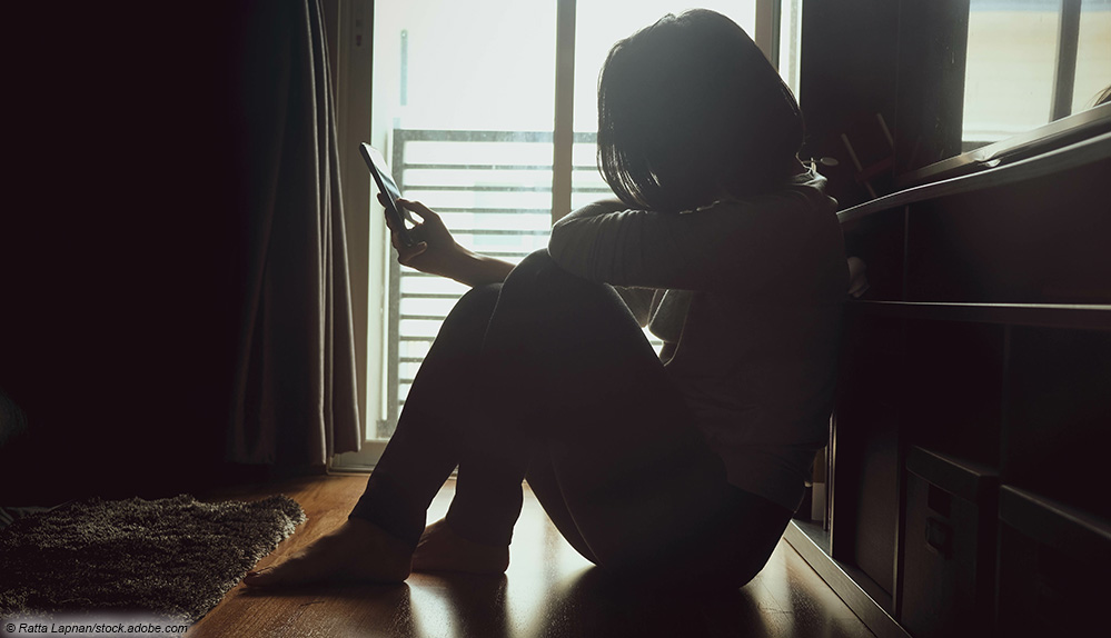 Frau sitzt mit Handy vor dem Fenster