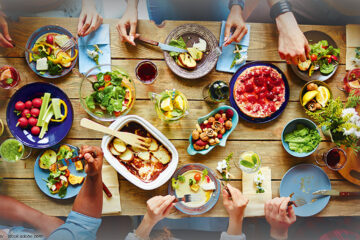 reich gedeckte Dinnertafel mit Gem&uuml;se und Freunden, die gemeinsam essen