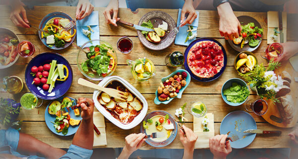 reich gedeckte Dinnertafel mit Gem&uuml;se und Freunden, die gemeinsam essen