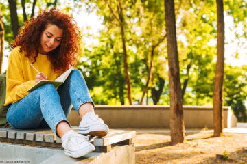 Frau sitzt im Park und schreibt ins Notizbuch