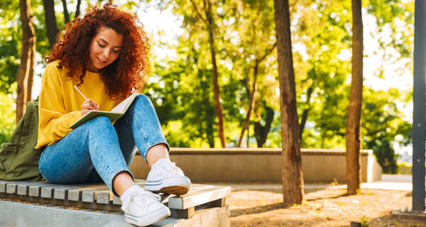 Frau sitzt im Park und schreibt ins Notizbuch