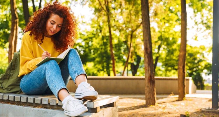Frau sitzt im Park und schreibt ins Notizbuch
