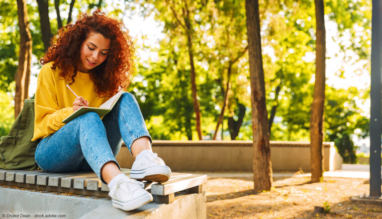 Frau sitzt im Park und schreibt ins Notizbuch