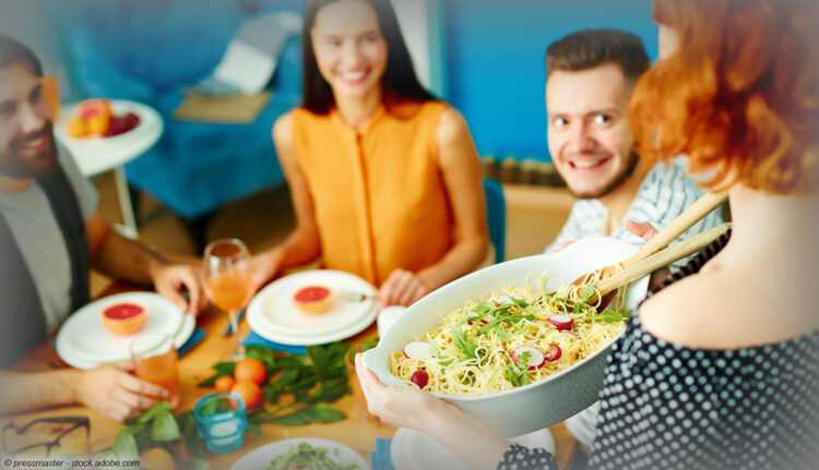 Freunde blicken freudig auf servierten Nudelsalat