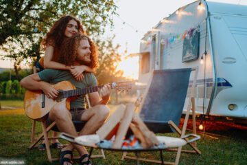 Paar vor Camper mit Gitarre und Lagerfeuer