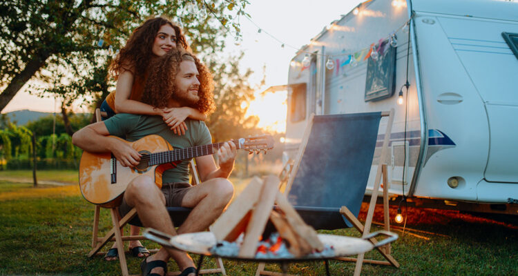 Paar vor Camper mit Gitarre und Lagerfeuer