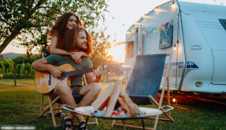 Paar vor Camper mit Gitarre und Lagerfeuer